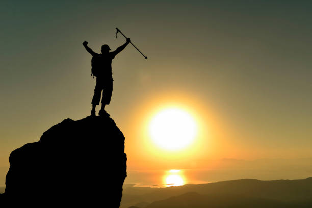 silhouette of professional mountaineer achieving summit achievement at magnificent sunrise stock photo