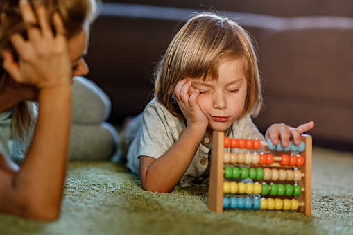 Cute boy feeling tired while learning to count on abacus with his single mother at home.