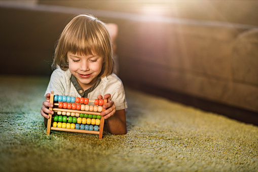 Preschool boy relaxing on carpet at home and learning to count on abacus. Copy space.