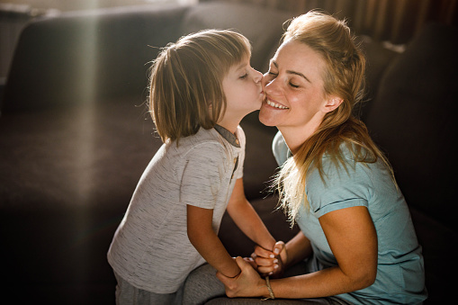 Loving mother and her small boy embracing with closed eyes at home while son is kissing mother. C