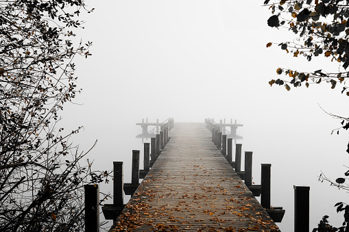 Jetty in the fog. Mystical foggy landscape at the lake. Morning fog in autumn.