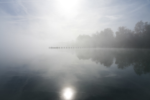 Landscape with a jetty at the lake. Nature with fog in the morning.