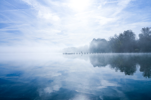 Jetty at the lake in the fog. Misty landscape in the morning. Idyllic nature by the water. Rest and relaxation.