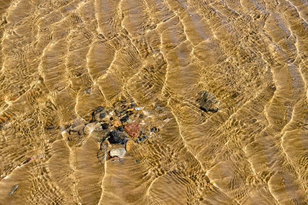 The stones lie on the yellow sand in the sea under clear water. The ripples from the waves are reflected on the bottom on a sunny day. Spain