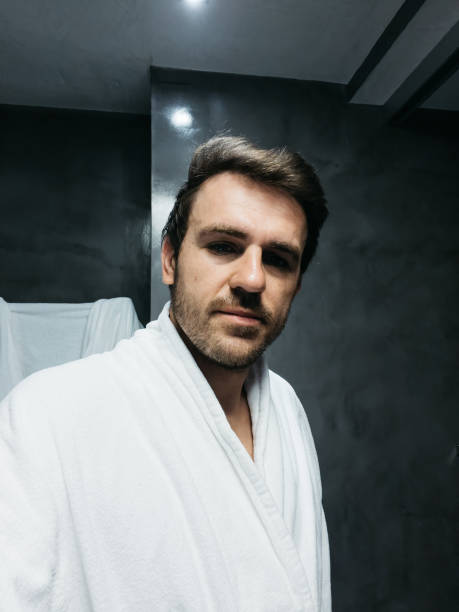 istock Young man in a white bathrobe is standing in the bathroom 1488770411