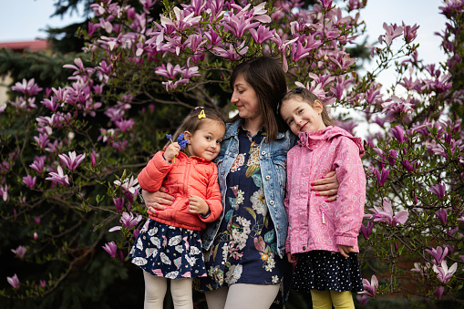 Happy Mother's Day. Mother with two daughters enjoying nice spring day near magnolia blooming tree.