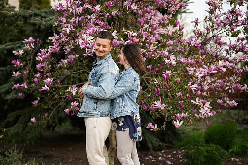 Tender couple in love wear jeans jacket enjoying nice spring day near magnolia blooming tree.