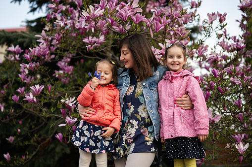 Happy Mother's Day. Mother with two daughters enjoying nice spring day near magnolia blooming tree.