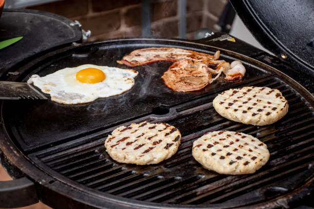 istock Burger patty, eggs and bacon grilling on barbecue grill plate . Backyard BBQ grill cooking burgers. 1488772389