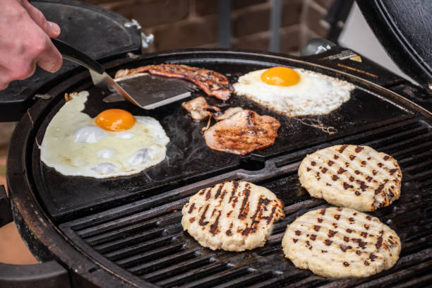 istock Burger patty, eggs and bacon grilling on barbecue grill plate . Backyard BBQ grill cooking burgers. 1488772431