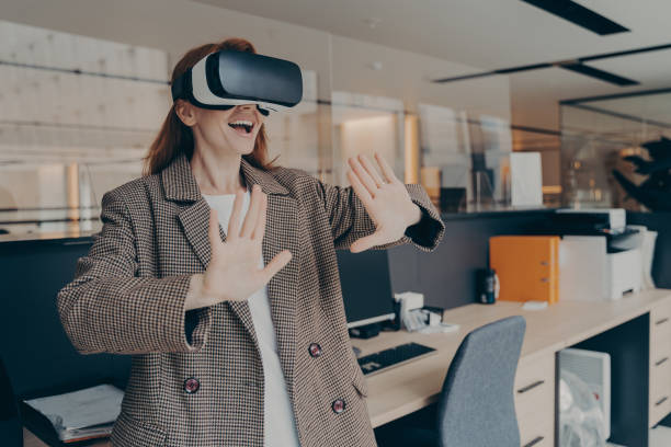 istock Woman wearing VR headset having fun in virtual reality game while standing in office 1488773810