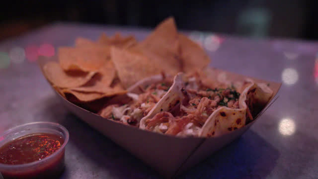 Slow-Motion Close-Up Shot of Unique Fish Tacos with Fried Onions from a Fast Food Truck or Local Business Taco Shop in San Diego under Vibrant-Colored Christmas Lights