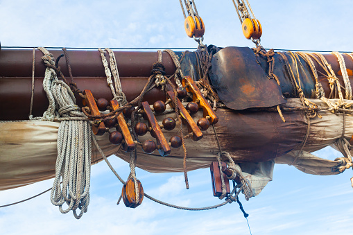 Part of an old, wooden sailing ship with a mast, folded sail and stretched sail ropes.