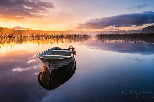 An awe-inspiring sunrise reflects off the tranquil lake, illuminating a row boat in its majestic beauty.