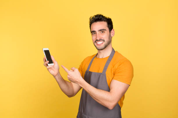 istock Smiling young man pointing at phone on yellow background 1488783708