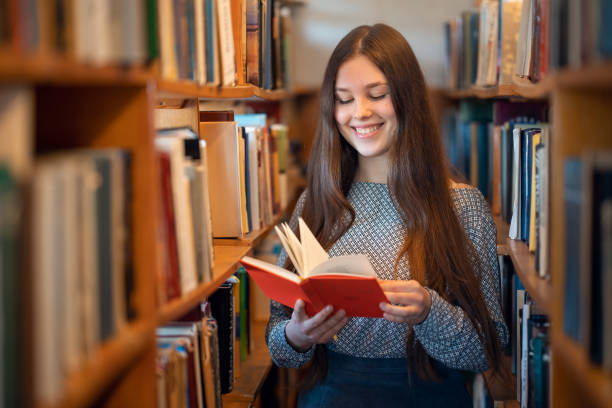 istock Cheerful female student standing between bookshelves in library of university during break between lesson 1488783845