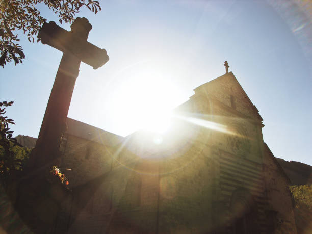 The photo shows a stone cross and a church silhouette from a low angle, creating a unique view of these religious icons. The cross towers over the frame, while the church stands out against the clear blue sky. The church’s architecture points to the sky, as if inviting the faithful to approach the heavens. The sunlight in this photo evokes the idea of divine light. It illuminates the cross and the church, making them glow with a special brightness, as if they are filled with the light of God. The low angle view makes the viewer feel awe and wonder, as if they are gazing up at these symbols of faith from a respectful and humble position. It’s a photo that encourages contemplation and reflection, asking the viewer to think about the deeper significance of these religious icons and their role in our world.