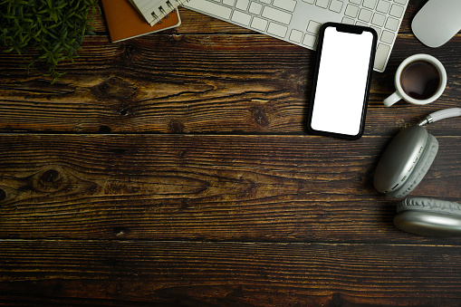 Top view of smartphone with empty screen, headphone, coffee cup and keyboard on wooden working desk. Copy space for text.