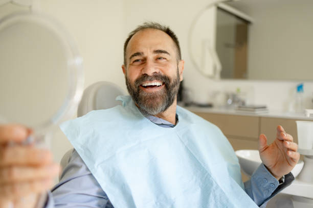 istock Happy man looking his teeth in a mirror at the dentists'. 1488785697