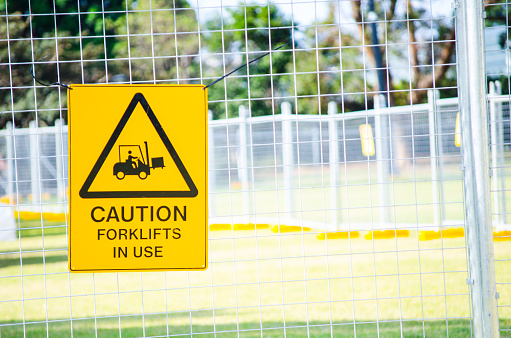 Yellow Caution sign for forklifts in use attached to the steel fence.