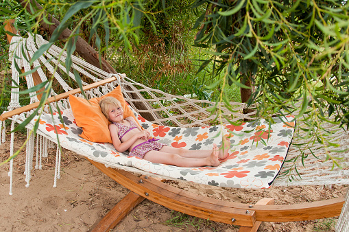 Summer beach tropical vacation with kids. Cute happy little caucausian girl rest laying in a hammock