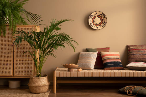 istock Warm and cozy ethno living room interior with couch, patterned pillows, plants i flowerpots, fern, rattan sideboard, basket on wall, wooden bowl and personal accessories. Home decor. Template. 1488794196