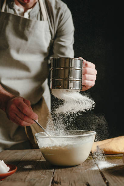 istock Unrecognizable man in an apron sifting and pouring flour into a bowl preparing dough 1488796355