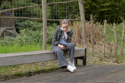 Sad message on the phone. A sad girl on a park bench reads a sad message from someone