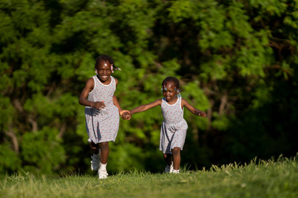 Rear view of playful sisters having fun while holding hands and running through nature.