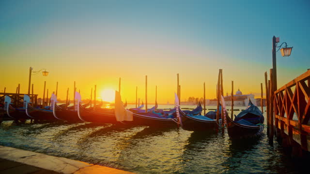 SLO MO shot of gondolas moored at canal. Boats by jetty against sky. Exploring city at sunset.