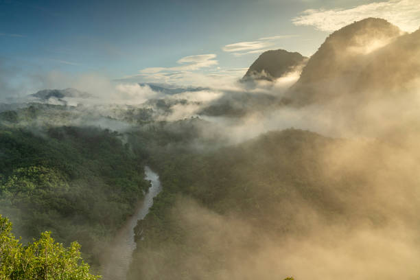 a scenic view of river, layered mountains or hill covered with golden light from the sunrise in a tropical rainforest stock photo