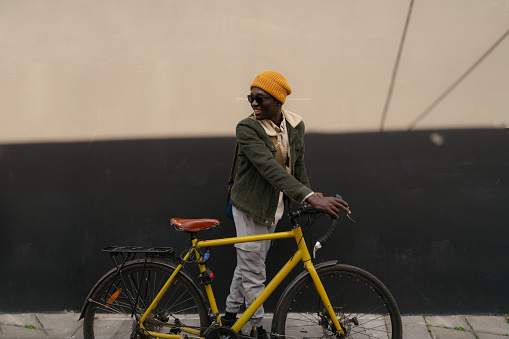 Photo of a young African - American man, pushing his bicycle down the busy street while commuting to work