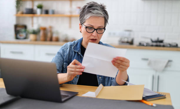 shocked woman holding letter in home interior, high bill for payment. - news of the world imagens e fotografias de stock