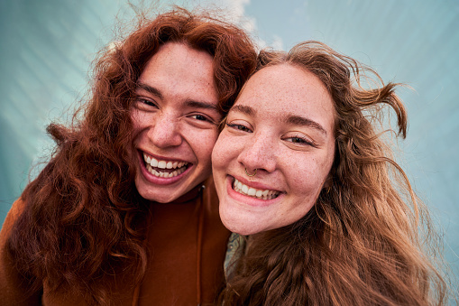 Cheerful close up portrait of two people putting the heads together looking at camera with big smile. Blonde girl and ginger boy taking a selfie.