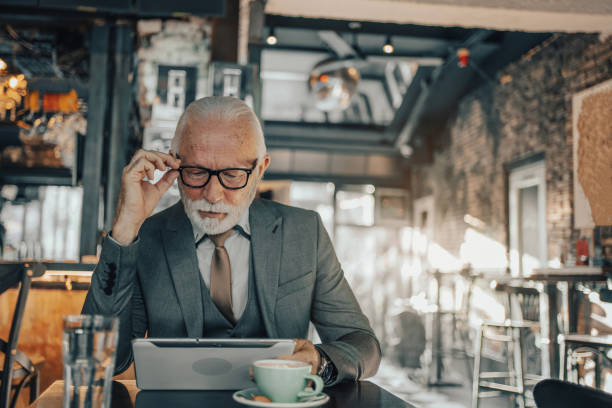 istock Mature business man, elegantly dressed, sitting in a coffee shop, focused and engaged while working online on a digital tablet, talking to clients or reading emails 1488809850