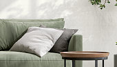 Round wooden coffee table podium, black steel leg, sage green suede leather sofa, cushion pillow in sunlight on concrete wall