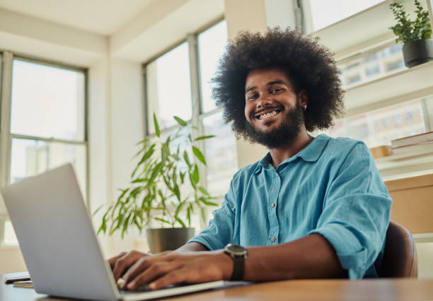 istock Happy, young black man with an afro typing on his laptop computer whilst working in an airy office environment 1488813349