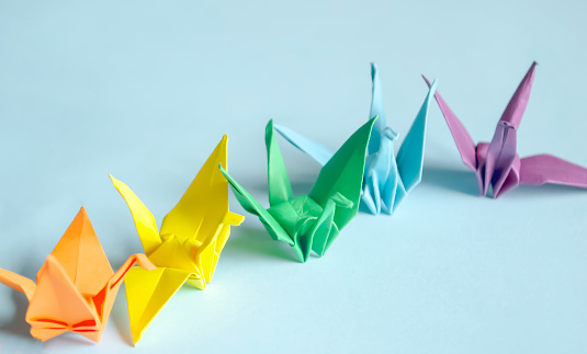 Paper cranes on a blue background. Four paper cranes stand in a row on a blue table, Japanese origami - paper cranes for the fulfillment of desires.