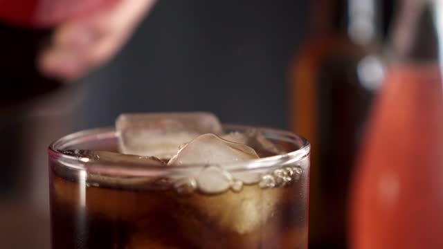 A carbonated soft drink is poured into a glass with ice cubes. Glass on a black background is filled