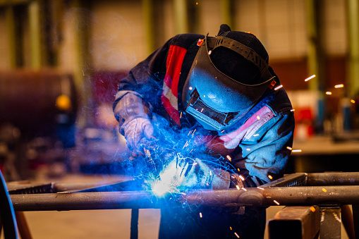 A welder welding two pieces of metal together in a metal fabrication facility.