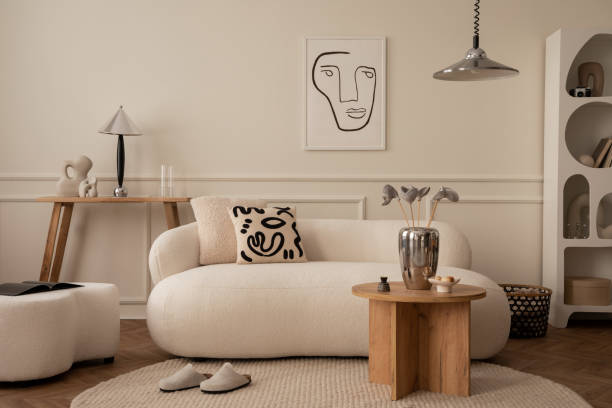 istock Creative composition of living room interior with mock up poster frame, white sofa, patterned pillow, wooden coffee table, stylish pouf, chrom lamp and personal silver accessories. Home decor Template 1488819349