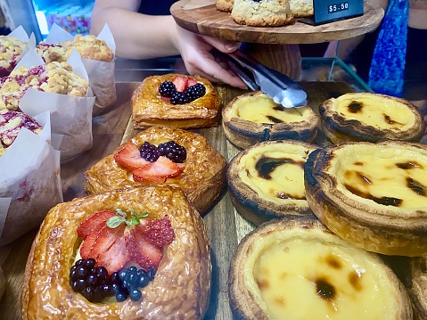 Horizontal close up of fresh made fruit flan, Portugese tarts and muffins in country pastry desert bakery Australia