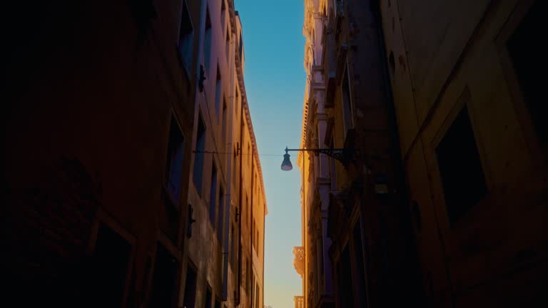 Tilt up shot of narrow alley amidst buildings. Silhouette birds on walkway at sunset. Exploring city.