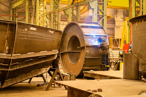 Male worker welding steel, sparks from light, protective masks and gloves increase safety