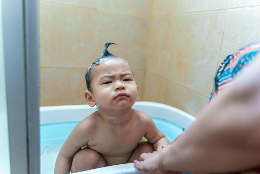Young cute Asian baby boy crying when taking a bath and wash hair by his mother. Baby son daily take care lifestyle hygiene parent relation concept. Parent taking care for infant at home. Family lifestyle parent connection affectionate concept.