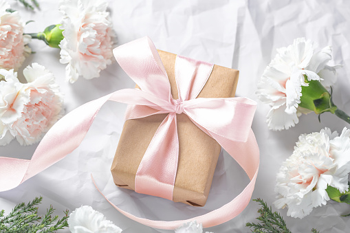 Gift box with pastel pink bow and carnation flowers on crumble paper background