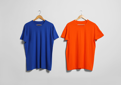 Hangers with different t-shirts on light wall. Mockup for design