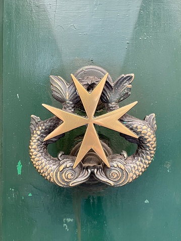 Close-up of a brass Maltese door handle and knocker in shape of Maltese cross and two fish