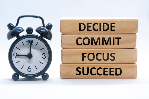 Decide, commit, focus, succeed text on wooden blocks with alarm clock on white cover background.