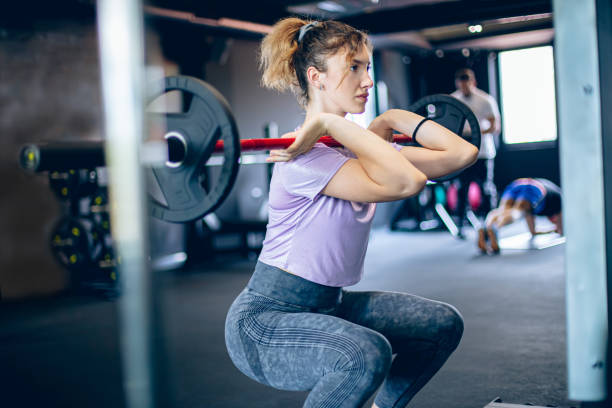 istock Young woman doing squats with barbell in gym 1488825870